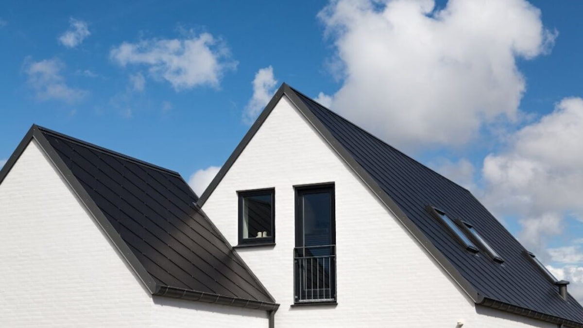 Een donker zadeldak op een witte woning met donkere kozijnen. Het contrast steekt mooi af tegen de helderblauwe lucht.