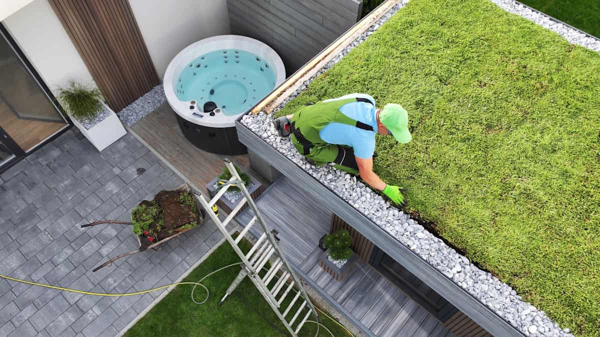 Een specialist legt een groendak aan op een tuinhuis. Het groendak bestaat uit gras omringd door grind om het regenwater af te voeren.
