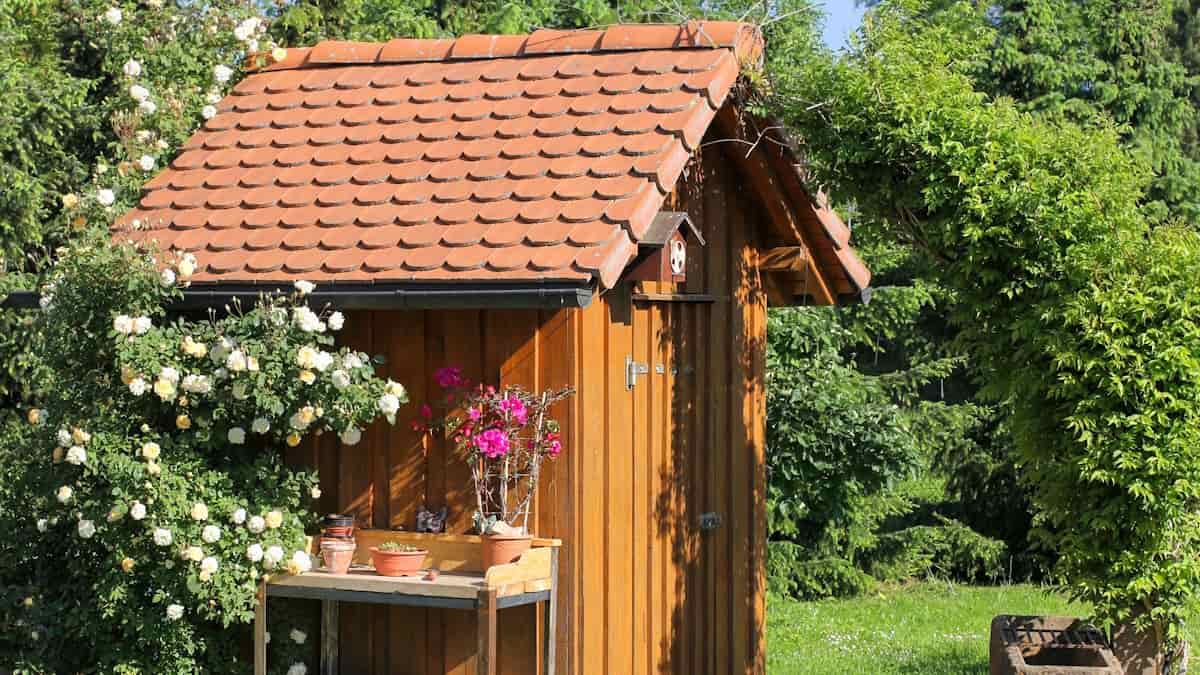 Een houten tuinhuisje met een leien dak in een groene omgeving. De leien zijn oranje van kleur.