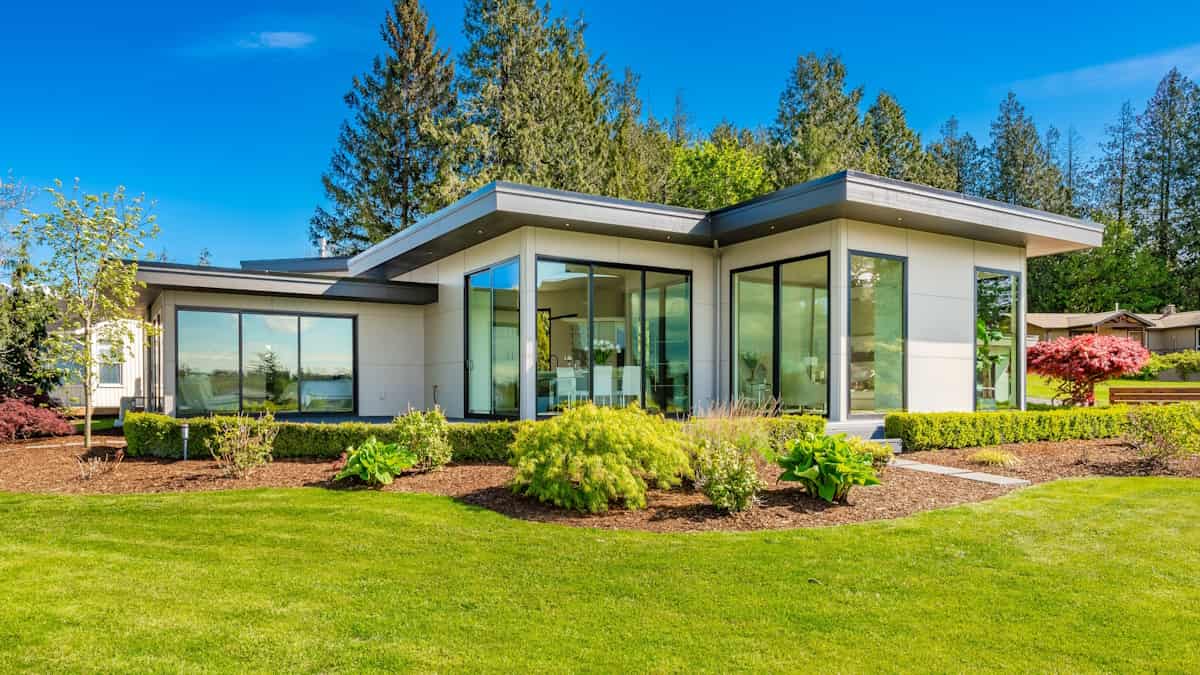 Een moderne woning met een plat dak in een groene omgeving. De woning is voorzien van grote raampartijen.